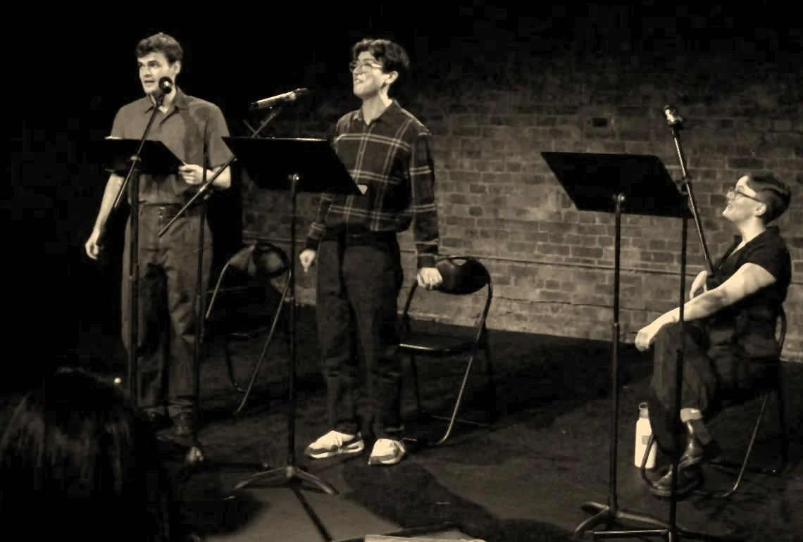 Charlie Renwick as Siegfried Sassoon and Josh Liew as Wilfred Owen standing at microphones, with Maddie Gray as the Witness seated on the right.